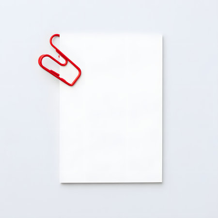 Blank white paper sheet held by a bright red binder clip on a neutral gray backgroundの素材