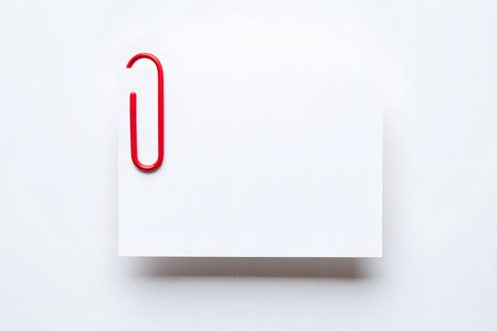 Bright red binder clip secures a blank white note card against a vibrant blue backgroundの素材