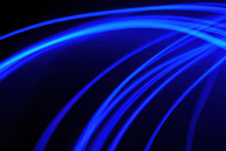Vibrant blue light streaks curve and flow across a deep black background, creating a dynamic abstract pattern.の素材