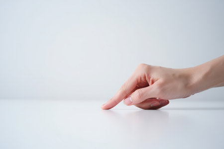 A person's hand gently touches a white surface with their index finger.の素材