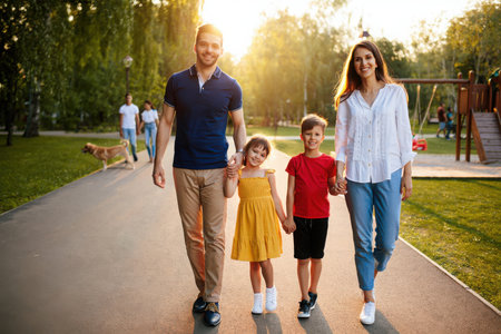 A smiling family of four walks together on a park path during golden hour.の素材