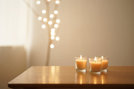 Three lit votive candles in glass holders on a wooden table.の素材