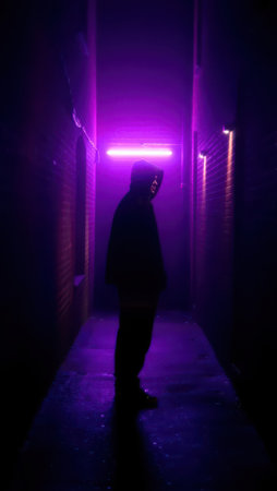 Silhouette of person in hoodie in purple neon alley.の素材