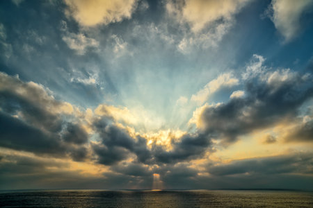 Sunset over the sea with sun beams through cloudsの写真素材