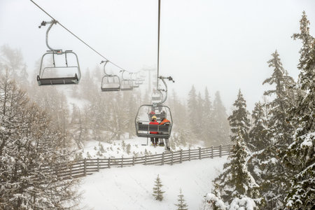 Chairlift with skiers in snowfall at alpine ski resortの写真素材