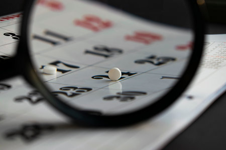 Conceptual photo with pills under a magnifying glass. White pills on a calendar background.