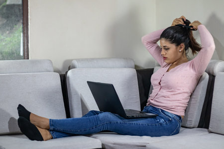 Woman picking up her hair while working from the sofa at homeの写真素材