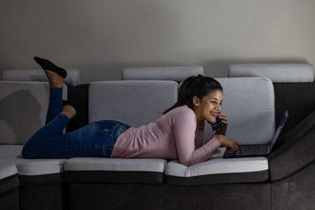 Smiling Woman Talking On Mobile Phone While Lying Down On Sofa At Homeの写真素材