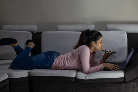 Woman Talking On Mobile Phone While Lying Down On Sofa At Homeの写真素材