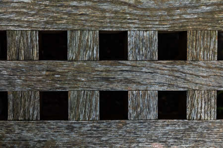 Brown wood fence texture with vertical and horizontal bars or planks and black square gaps between...