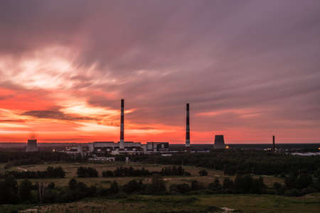 The thermal power station with pipes or tubes and cooling towers in Lavriki. The inustrial lanscape in the countryside in the rays of rising or setting sun with the trees and bushes in the white nightの写真素材