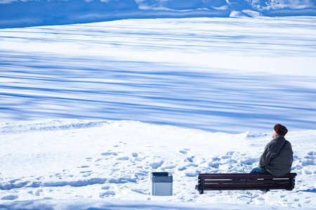 Beautiful vivid, colorful and bright landscape of winter park with alone old man sitting on the bench and sunbathing in rays of spring or winter sunの写真素材