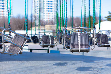 Vivid, colorful and bright urban background, scenery or view of modern carousel or roundabout with seats on chain suspensions in city park in summer or spring sunny weatherの写真素材