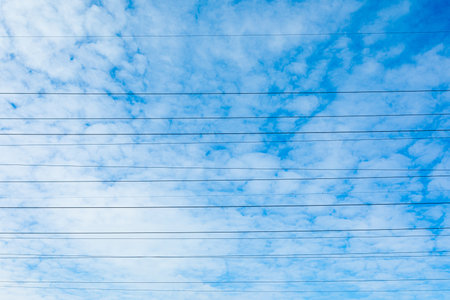 Beautiful bright, vivid and colorful horizontal background or backdrop of blue sky and white clouds with silhouettees of wires of electrical main or transmission line in sunny dayの写真素材