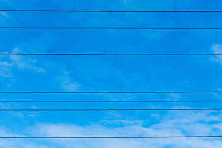 Beautiful bright, vivid and colorful horizontal background or backdrop of blue sky and white clouds with silhouettees of wires of electrical main or transmission line in sunny dayの写真素材