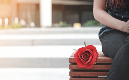 The roses were place beside that girl sitting waiting for someone at the Brown wooden chairs.の写真素材