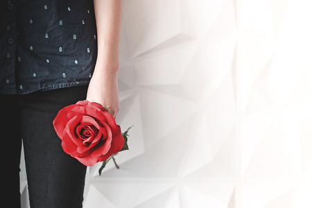 Young woman holding a red rose in her hand, waiting for someone to come looking for her.の写真素材