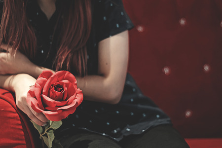 Young woman holding a red rose in her hand, waiting for someone to come looking for her.の写真素材