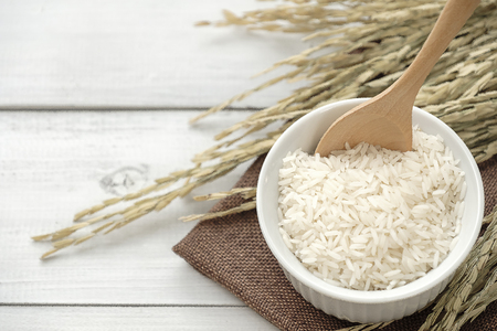 Rice in white bowl with yellow rice plant on wooden background.の写真素材