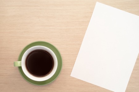 A green cup of coffee on the background of a table and a white sheet of paper simulates the beginningの写真素材