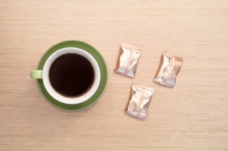 Green cup of coffee on the background of the pink wood table and three sweets. View from topの写真素材
