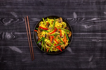 Appetizing stir fried noodles with garlic sprouts, mushrooms, red pepper and chicken meat on a black...
