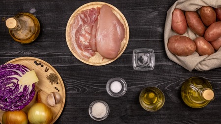 Fresh ingredients for cooking fried potatoes, stewed cabbage and grilled sausages or chevapchichi based homemade recipes on a black rustic wooden table. Top view.の写真素材