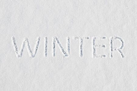 The word winter written in fresh snow at the threshold of the end of autumn and before the start of the New Year and Christmas holidaysの写真素材