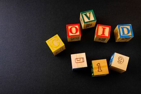 Wooden alphabet cubes on COVID-19 over dark surface. Focus on selective cubes. Conceptual of...