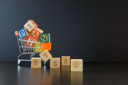 Conceptual of panic buying of food or groceries during virus outbreak lock down or serious crisis. Wooden cubes  overloads on mini trolley cart over dark and dusty surface. Focus of selective cubes.の写真素材
