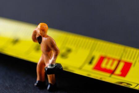 Conceptual of social distancing during movement control order to control virus outbreak.  Single worker at 1 meter mark yellow measuring tape. Selective focus on figurine on left.の写真素材