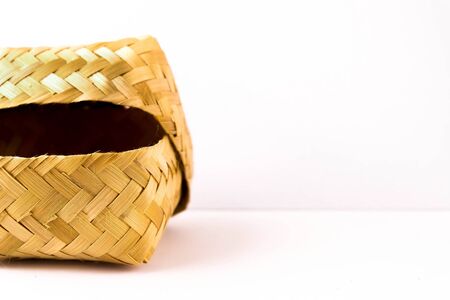 Close-up small hand-woven bamboo wicker container with lid partly opened over white. Selective focus on container. Usually use for food storage.の写真素材
