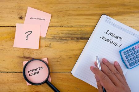 Image of magnifier pen sticky notes calculator and note book over wooden table. Conceptual of impact analysis from outbreak conflict or crisis. Selective focus.の写真素材