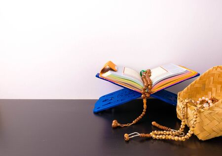 Muslim prayer beads on opened quran with purple cover on fordable book rest. Beads in wicker basket...