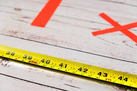 Yellow measuring tape with red social distancing table marker on seating gap for dine-in at restaurants or cafes. Conceptual  image. Wooden table. Selective focus on measuring tape.の写真素材