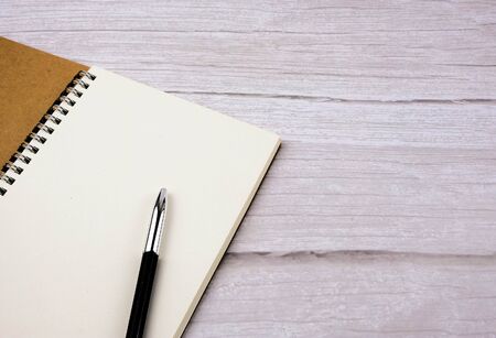 Blank spiral note book with pen over wooden table. Top view of minimalist workplace image with copy...