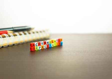 Conceptual of accumulated depreciation in financial statements. Colorful alphabet beads stacked forming the words over dark table. Spiral notebook and pencil visible. Focus on text on beads at front.の写真素材
