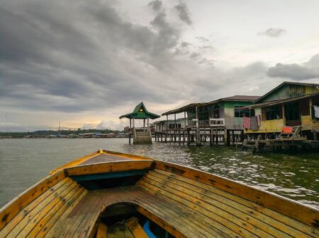 Image of wooden houses at water village at bandar seri begawan brunei from a moving boat. Gloomy rain-bound  cloud at backgroud. Focus of wooden houses. Noise or grain due to extreme gloomy condition.の写真素材