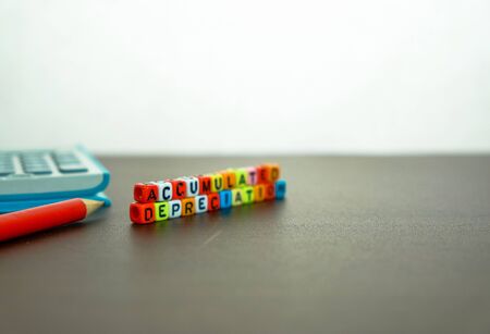 Conceptual of accumulated depreciation in financial statements. Colorful alphabet beads stacked forming the words over dark table. Spiral notebook and pencil visible. Focus on text on beads at front.の写真素材