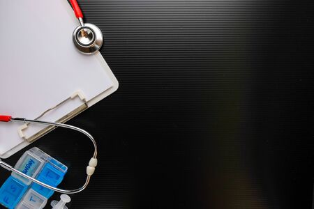 Top view low key conceptual of corona virus outbreak alert. Mini chalkboard, red stethoscope, medicine tablets and syringe on white  paper over dark surface. Focus on chalkboard.の写真素材