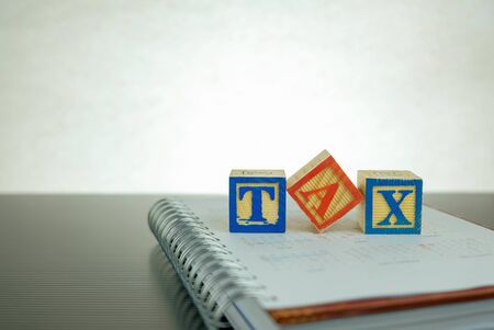 Conceptual image of annual tax return. Stacked wooden block letter forming TAX on dark reflective...