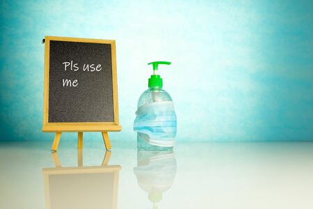 Hand sanitizer covered by face mask besides chalkboard over blue background. Conceptual of keeping sanitized hands and wearing face mask. Selective focus.の写真素材