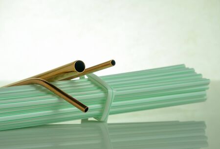 Conceptual of world issue on single use plastic against reusable steel straw. Steel straws in empty glass on reflective table.Selective focus at straws at center. Plastic straws in visibility.の写真素材