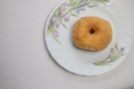 Donut on the white plate on the white tablecloth background.