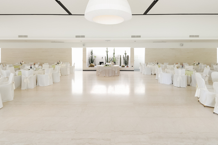 Table of the couple in the middle and tables of guests at the sides in a white room set up for the event to understand a concept of life with loveの写真素材