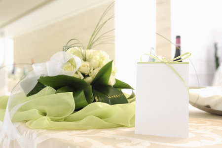 Placeholder with green ribbon on a table with a bouquet of white roses in the background to understand the concept of celebrationの写真素材