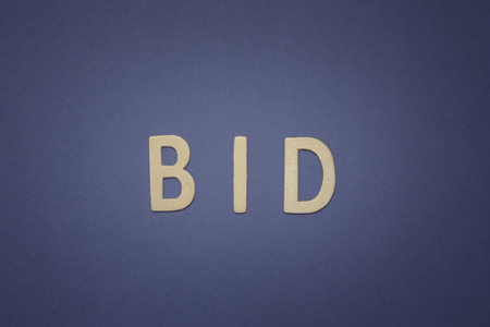 Bid written with wooden letters on a blue background to mean a business conceptの写真素材