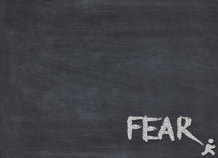 The word fear in chalk on blackboard with little man running away. Conceptualの写真素材