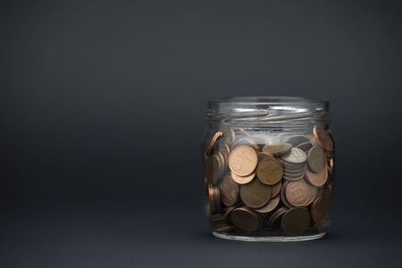 Glass jar with coins on black table, space for text