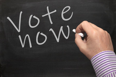 A hand writing a white Vote Now text on a black backgroundの写真素材